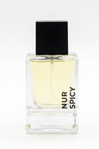 A clear glass perfume bottle with pale yellow liquid, a black rectangular cap, and vertical black text reading 'NUR SPICY' on the front, shown on a white background.